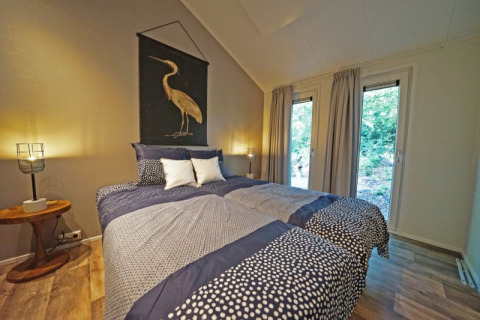 Knusse lodge slaapkamer met tweepersoonsbed, grote ramen met zicht op de natuur en modern interieur.
