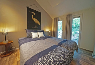 Knusse lodge slaapkamer met tweepersoonsbed, grote ramen met zicht op de natuur en modern interieur.
