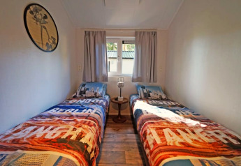 Lichte lodgekamer met twee enkele bedden, kleurrijke dekens, een klein tafeltje en een raam met gordijnen.