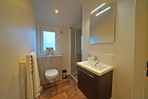 Modernes Badezimmer in einer Lodge mit Wandtoilette, Dusche, Waschbecken, Spiegel und Holzfußboden.