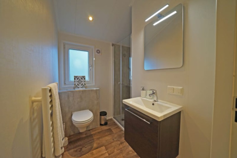 Moderne lodgebadkamer met zwevend toilet, douche, wastafel, verlichte spiegel en vloer in houtlook.