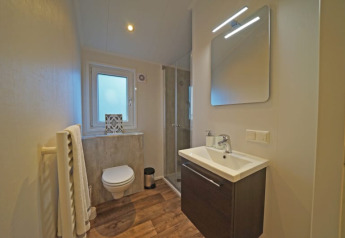Moderne lodgebadkamer met zwevend toilet, douche, wastafel, verlichte spiegel en vloer in houtlook.