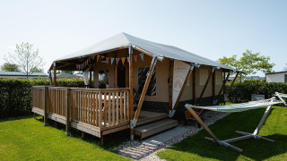Lodge Villatent Cottage con porche de madera y hamaca en Camping de Molenhoek, Países Bajos, día soleado.