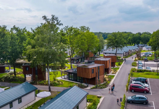 Luchtfoto van een vakantiepark met moderne glampingaccommodaties, omgeven door groen en parkeerplaatsen.