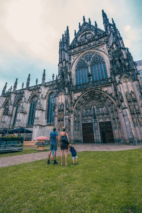 Een gezin staat voor een indrukwekkende gotische kathedraal bij een vakantiepark met glamping faciliteiten.