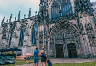 Een gezin staat voor een indrukwekkende gotische kathedraal bij een vakantiepark met glamping faciliteiten.