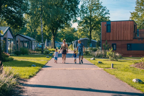 Gezin wandelt op een zonnige dag door een modern vakantiepark met glamping accommodaties en groene omgeving.