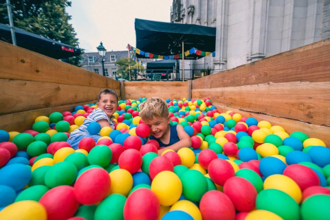 Twee kinderen spelen vrolijk in een ballenbak op een vakantiepark met glamping, omringd door kleurrijke ballen.
