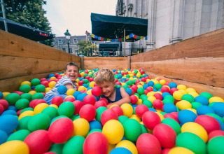 Twee kinderen spelen vrolijk in een ballenbak op een vakantiepark met glamping, omringd door kleurrijke ballen.