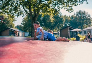 Twee kinderen spelen en lachen op een grote opblaasbare mat bij een glamping vakantiepark in de zomer.