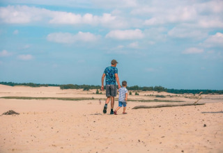 Vader en zoon wandelen hand in hand op een zonnige zandvlakte bij een vakantiepark met glamping.