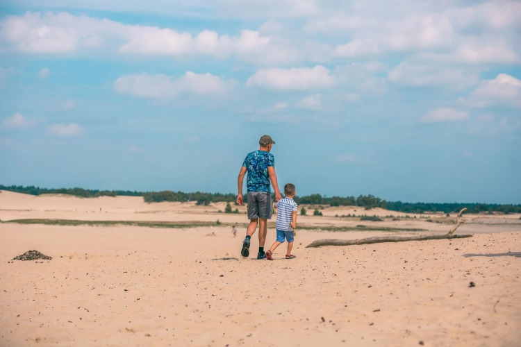 Vader en zoon wandelen hand in hand op een zonnige zandvlakte bij een vakantiepark met glamping.
