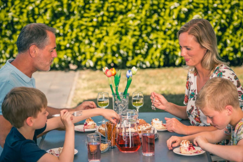 Gezin geniet samen van een maaltijd buiten aan een tafel in een vakantiepark met glamping accommodaties.