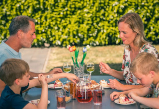 Gezin geniet samen van een maaltijd buiten aan een tafel in een vakantiepark met glamping accommodaties.