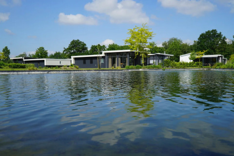 Vakantiepark met moderne glamping-accommodaties aan het water, omgeven door veel groen en natuur.
