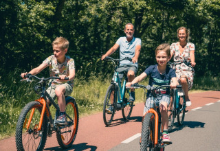 Gezin fietst samen op een zonnige dag over een fietspad in de natuur nabij een glamping vakantiepark.