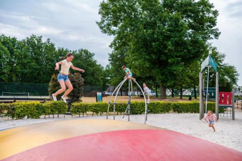 Kinderen spelen op een springkussen en klimrek in een gezinsvriendelijk vakantiepark met glamping.