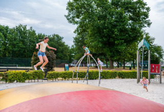 Kinderen spelen op een springkussen en klimrek in een gezinsvriendelijk vakantiepark met glamping.