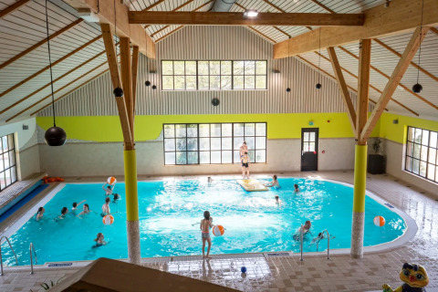 Kinderen spelen en zwemmen in een overdekt zwembad in een vakantiepark met glamping accommodaties.