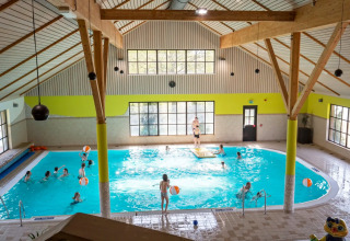 Kinderen spelen en zwemmen in een overdekt zwembad in een vakantiepark met glamping accommodaties.