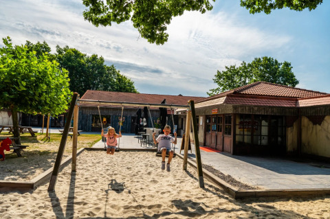 Kinderen spelen op schommels in een zandbak, gelegen bij een vakantiepark met glamping verblijf.