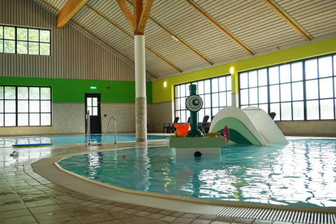 Overdekt zwembad met kinderspeeltoestellen en glijbaan in een vakantiepark met glamping accommodaties.