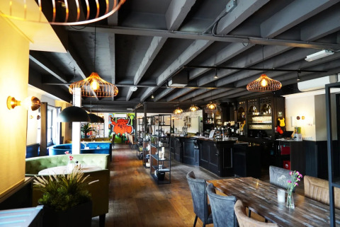 Modern, sfeervol restaurant met houten vloer, zithoeken, bar en kleurrijke muurschildering in een vakantiepark.