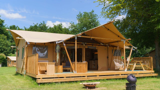 Glampingtent La Gran Vida in Resort de Parel, Nederland, met houten terras en hangstoel op het gras.