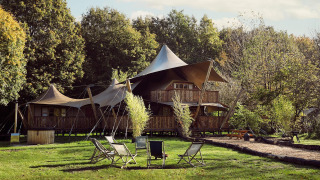 Sfeervolle glampingtent Hacienda bij Resort de Parel in Nederland, met ligstoelen en veel groen rondom.