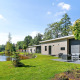Moderne Lodge Grand Modern ved en dam omgivet af grønt græs og træer under en blå himmel.