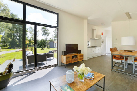 Moderne lodge met grote ramen, uitzicht op tuin, woonkamer en open keuken in Nederland.