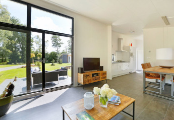 Moderne lodge met grote ramen, uitzicht op tuin, woonkamer en open keuken in Nederland.
