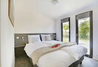 Moderne og lys dobbeltseng på Lodge Grand Modern i Holiday Park De Lochemse Berg med store vinduer.