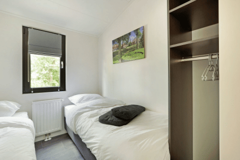 Kamer met twee eenpersoonsbedden, raam, open kledingkast en wanddecoratie in Lodge Grand Modern, De Lochemse Berg.