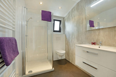 Baño moderno con ducha acristalada, inodoro, lavabo blanco y toallas moradas en Lodge Grand Modern, De Lochemse Berg.