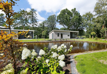 Moderne lodge met terras aan een vijver, omgeven door groen op Holiday Park De Lochemse Berg, Nederland.