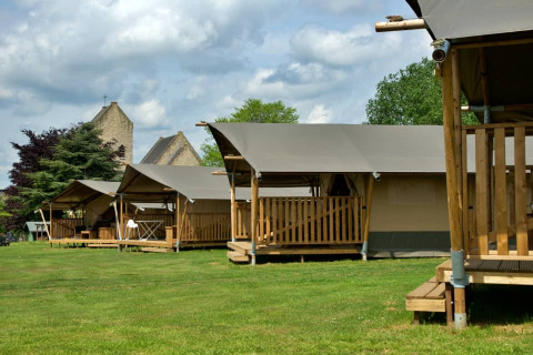 Safari tents at Camping La Dolce Vita in the Netherlands with wooden decks, lush grass, and cloudy sky.