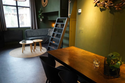 Moderne glampingaccommodatie met groene muren, sofa, ronde tafeltjes, eetruimte en ladder naar de mezzanine.
