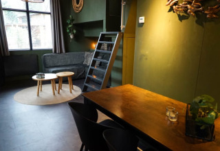 Stylish glamping accommodation with green walls, sofa, small round tables, dining area, and ladder to loft.