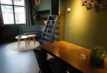 Alojamiento glamping elegante con paredes verdes, sofá, mesas redondas, área de comedor y escalera al altillo.