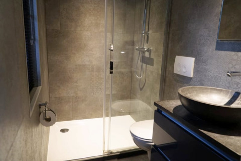 Modern bathroom at a glamping accommodation with shower, wall-mounted toilet, and stone sink bowl.