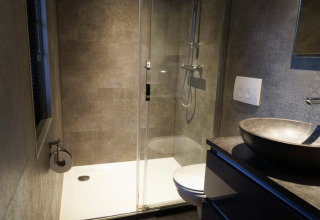 Bagno moderno in una struttura glamping con doccia, WC sospeso e lavabo in pietra.