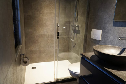 Baño moderno en alojamiento glamping con ducha, inodoro empotrado en la pared y lavabo de piedra.