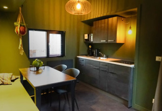 Moderne Glamping-Küche mit grünen Wänden, Esstisch, Hängepflanzen und eleganten dunklen Schränken.