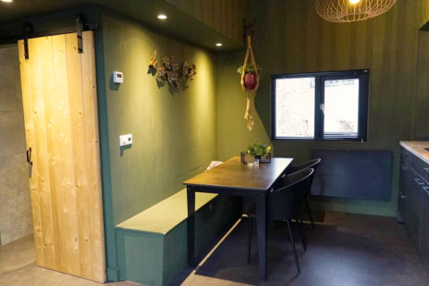 Modern glamping accommodation interior with green walls, sliding wooden door, dining area, and window.