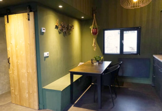 Modern glamping accommodation interior with green walls, sliding wooden door, dining area, and window.