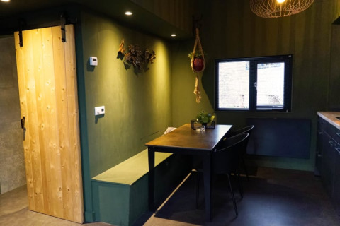 Moderne glamping-accommodatie met groene muren, houten schuifdeur, eethoek en raam met uitzicht.
