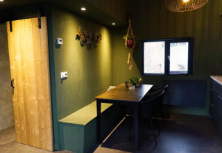 Moderne glamping-accommodatie met groene muren, houten schuifdeur, eethoek en raam met uitzicht.
