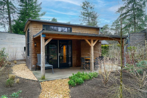 A cozy glamping accommodation with a covered wooden porch and outdoor seating, surrounded by nature.