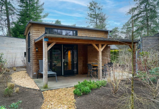 A cozy glamping accommodation with a covered wooden porch and outdoor seating, surrounded by nature.